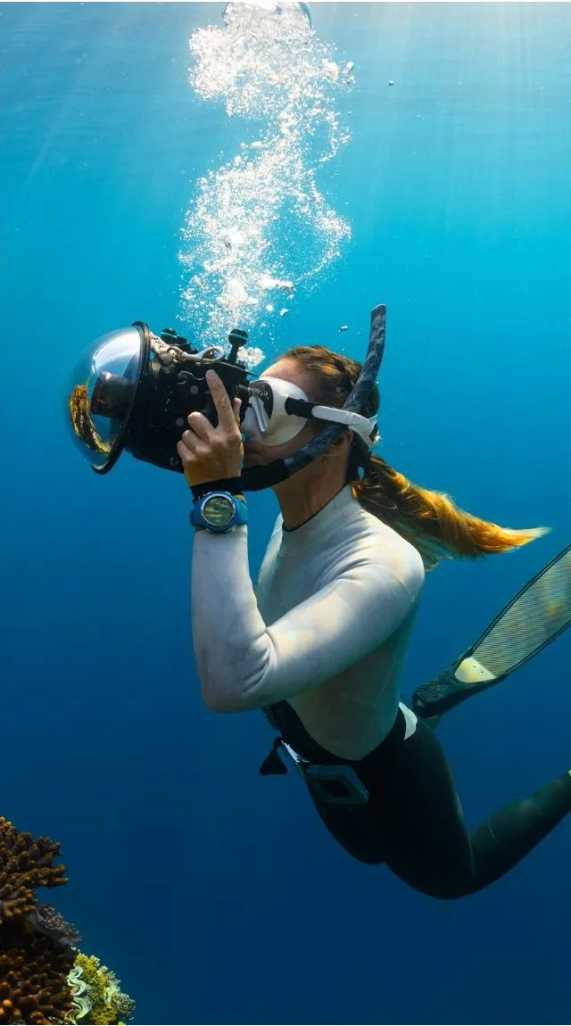 A freediver underwater, exhaling a column of bubbles toward the surface.