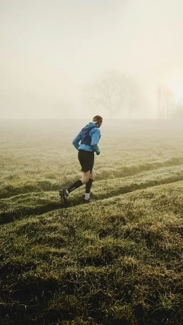 A trail runner crossing a misty field.